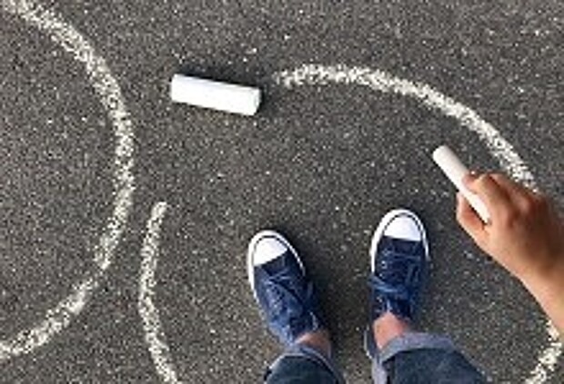Ein Kind malt einen Kreidekreis auf Asphalt