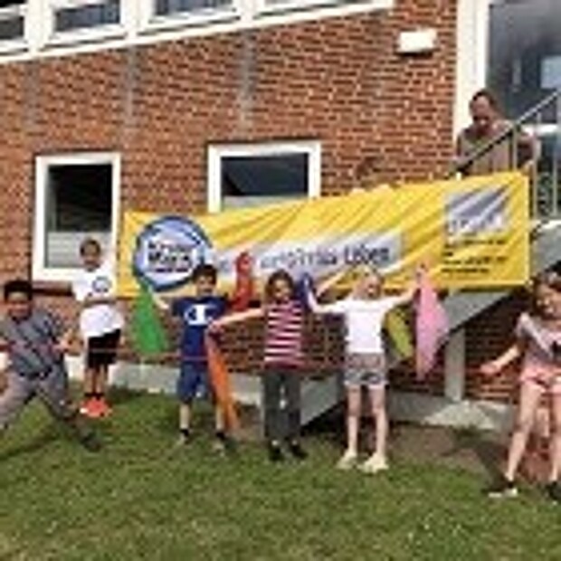 Kinder und eine Lehrerin vor einem "Kinder stark machen"-Banner