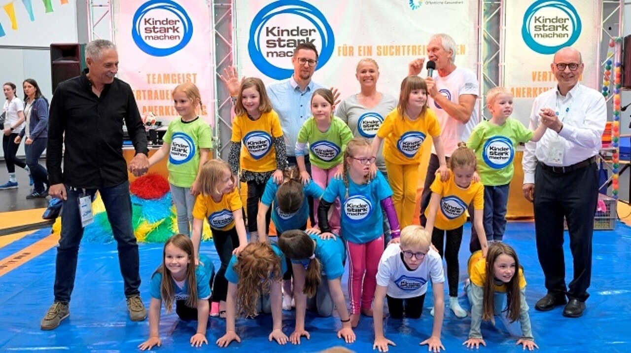 Kinder in bunten „Kinder stark machen“-T-Shirts bauen auf der Aktionsbühne eine Menschenpyramide. 