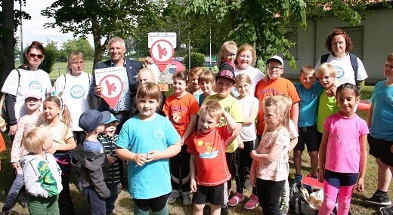 Kinder und Erwachsene stehen um das erste Schild der Bewegungshaltestellen herum