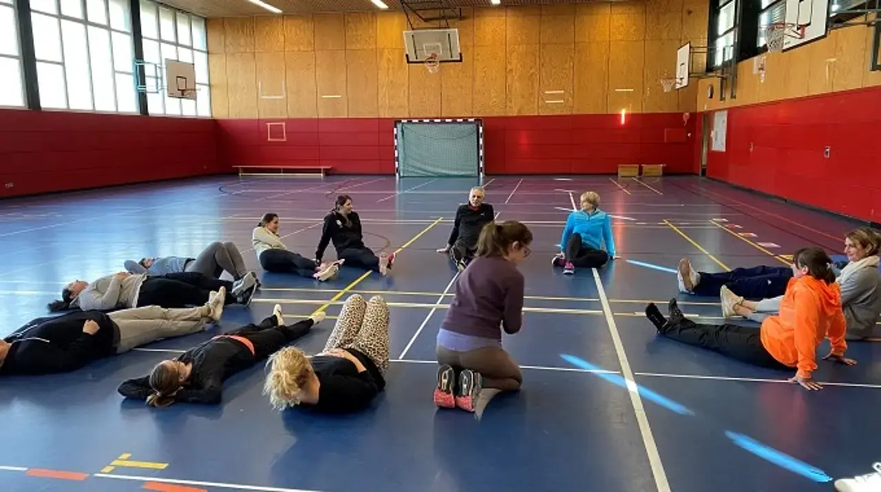 Die Teilnehmerinnen und Teilnehmer der Schulung mit Harald Schmid sitzen auf dem Boden der Turnhalle.