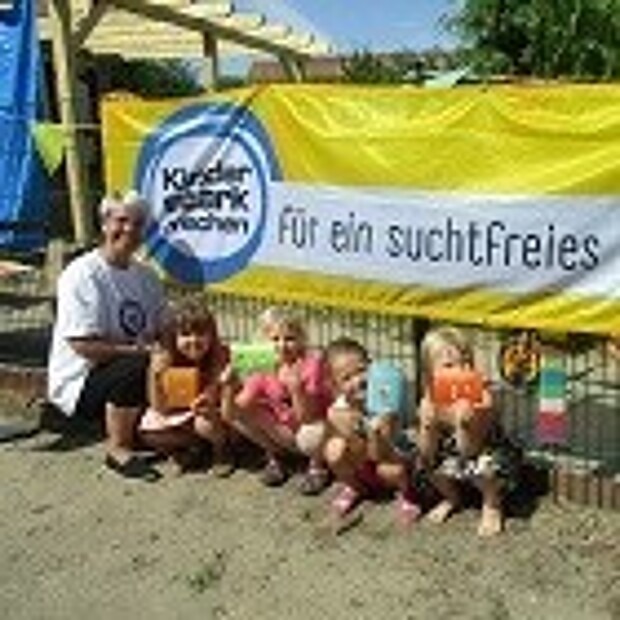 Kinder und eine Erzieherin der Kita Mühlenspatzen vor einem "Kinder stark machen"-Banner