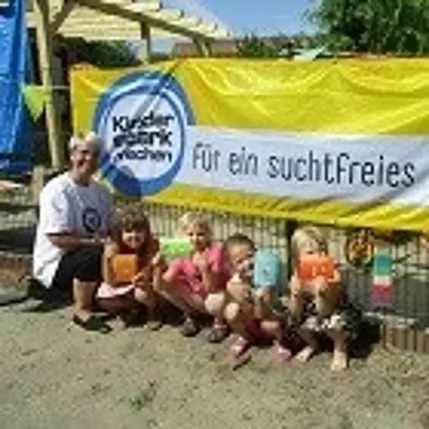 © Kita Mühlenspatzen Kinder und eine Erzieherin der Kita Mühlenspatzen vor einem "Kinder stark machen"-Banner