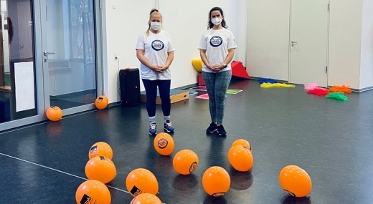 Vor zwei Erzieherinnen mit Maske und Kinder stark machen T-Shirt liegen Luftballons