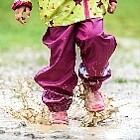 Ein Kind mit regenfester Kleidung und Gummistiefeln springt in eine Pfütze
