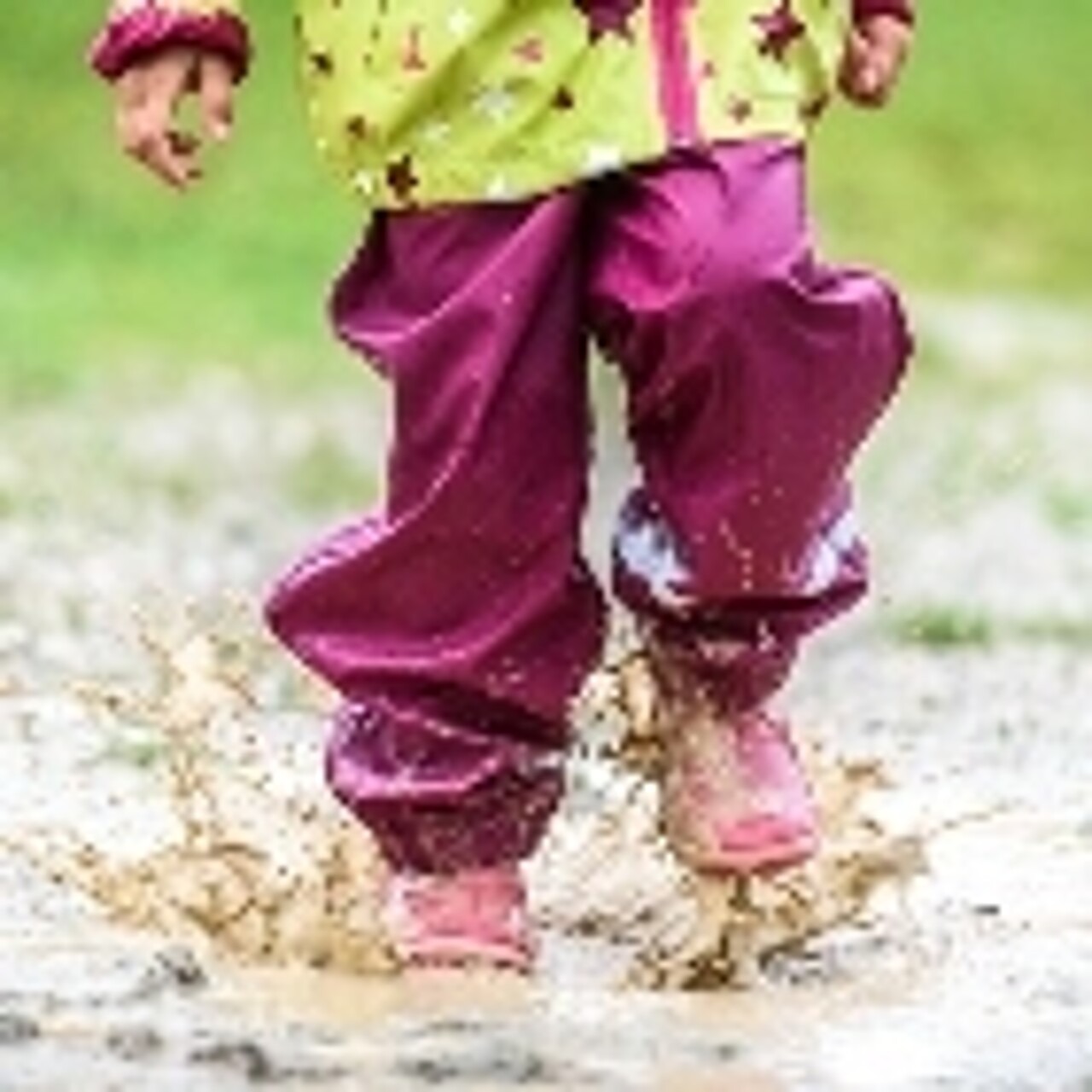 Ein Kind mit Gummistiefeln springt in eine Pfütze