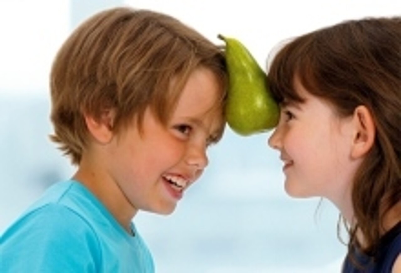 Ein Mädchen und ein Junge balancieren eine Birne zwischen ihren Stirnen