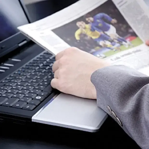 aufgeschlagene Zeitung mit einem Sportbild liegt auf geöffnetem Laptop