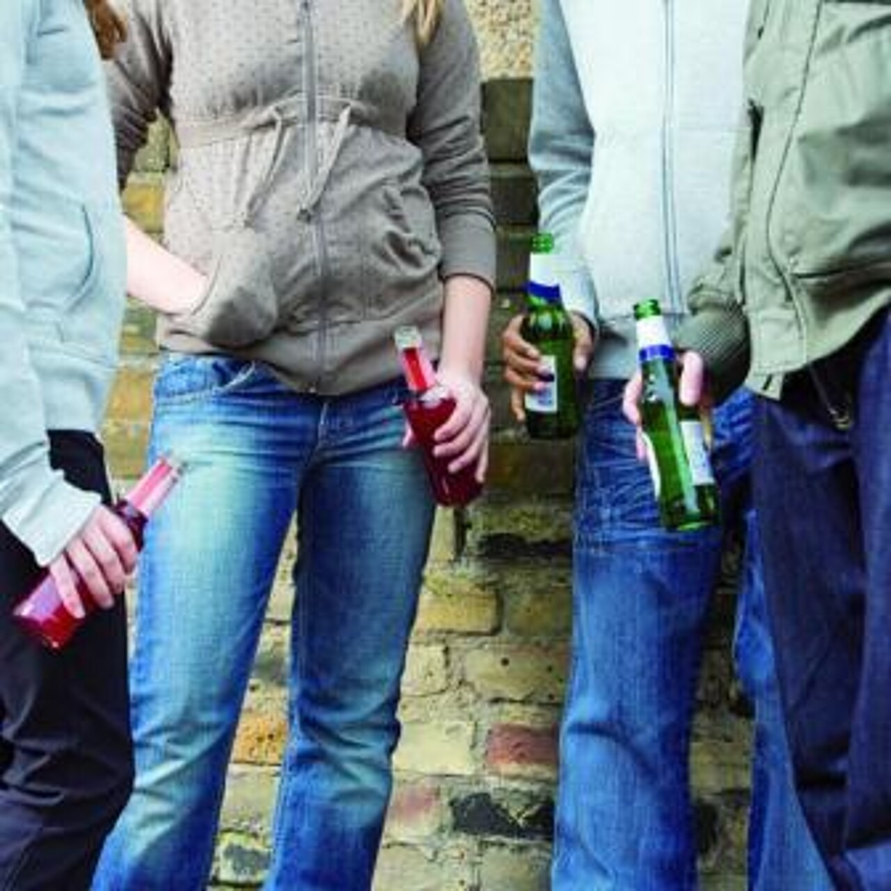 Eine Gruppe Jugendlicher mit jeweils einer Flasche Alkohol in der Hand steht vor einer Wand