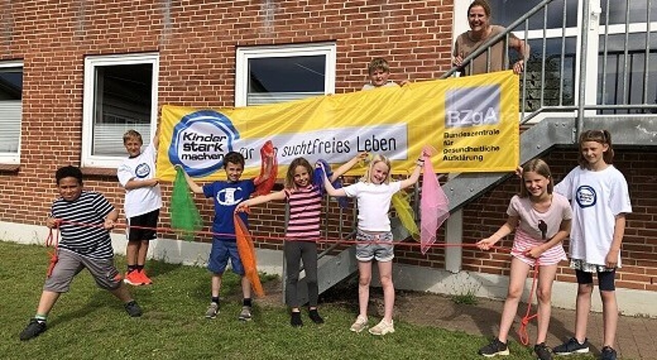 Kinder und eine Lehrerin vor einem "Kinder stark machen"-Banner