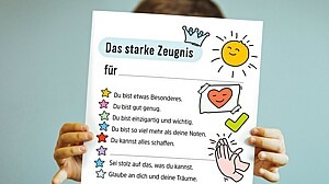 Kind hält Zeugnis mit wertschätzenden Botschaften vor sich.