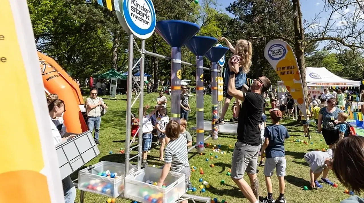 Vater nimmt Tochter hoch, um gemeinsam einen Ball in den Trichter des Meinungsbarometers zu werfen.