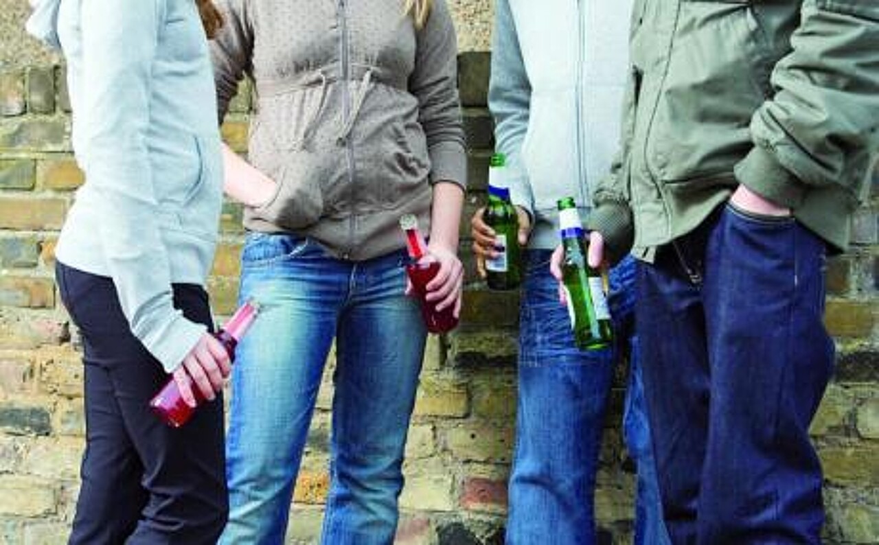 Eine Gruppe Jugendlicher mit jeweils einer Flasche Alkohol in der Hand steht vor einer Wand