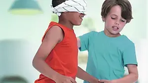 Ein Junge mit verbundenen Augen wird von einem anderen Jungen geführt.