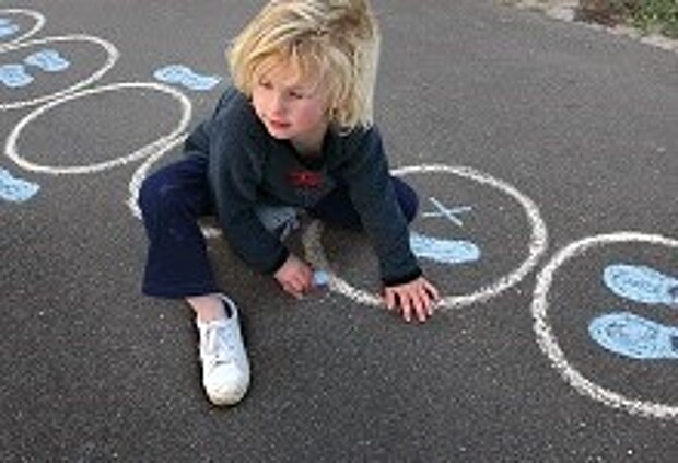Ein Kind malt mit Kreide einen Kreis auf Asphalt