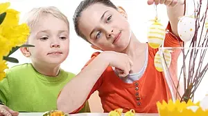 Ein Mädchen und ein Junge hängen Ostereier an Weidenkätzchen-Zweige in einer Vase.