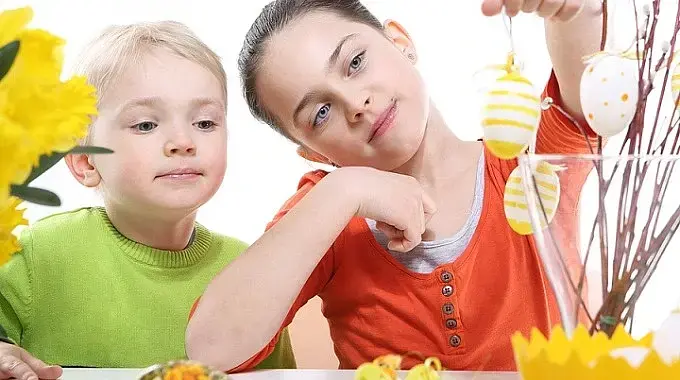 Ein Mädchen und ein Junge hängen Ostereier an Weidenkätzchen-Zweige in einer Vase.