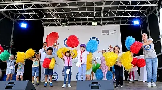 Singa und Kinder wedeln mit Cheerleading-Pompons auf der BZgA-Bühne.