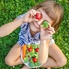Ein Kind hält sich eine Tomate und ein Stück Brokkoli vor die Augen