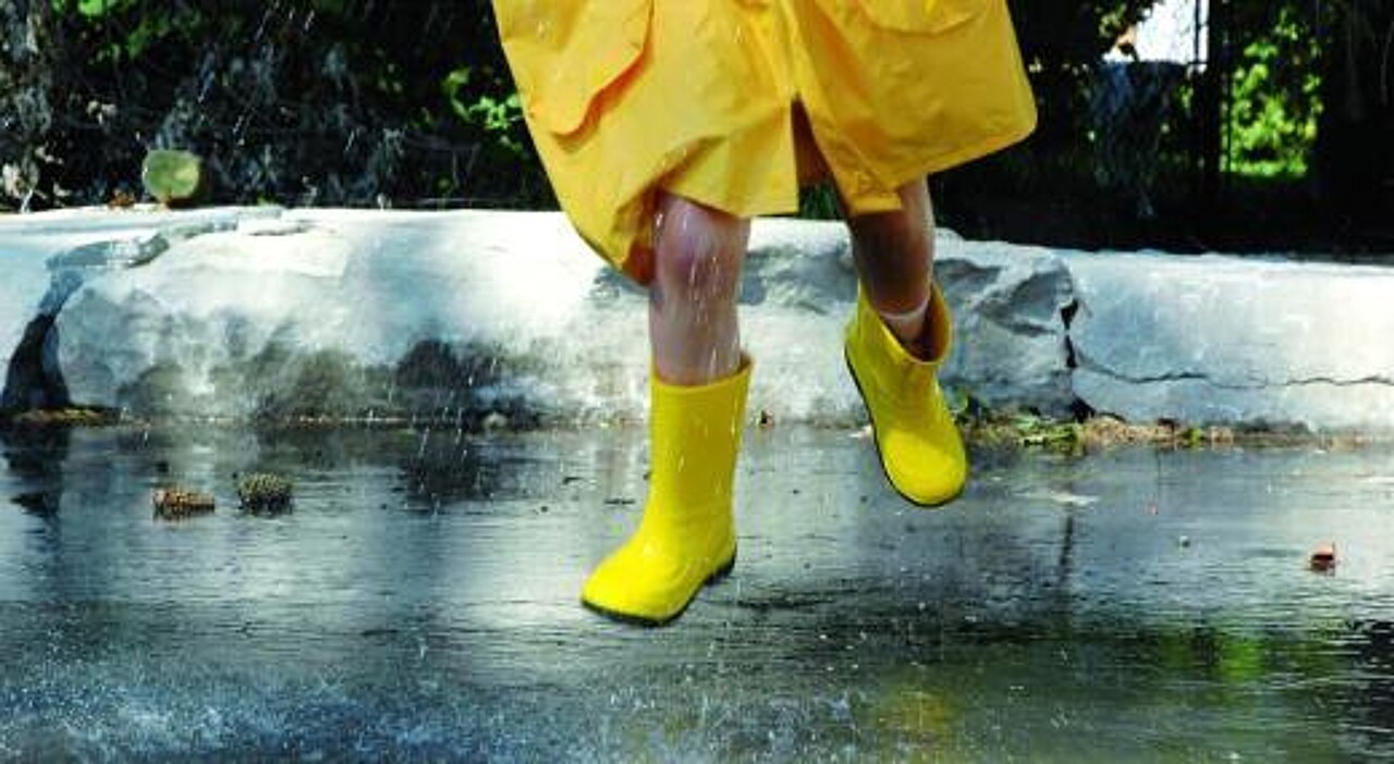 Kind in gelbem Regenmantel springt in gelben Gummistiefeln über eine Pfütze