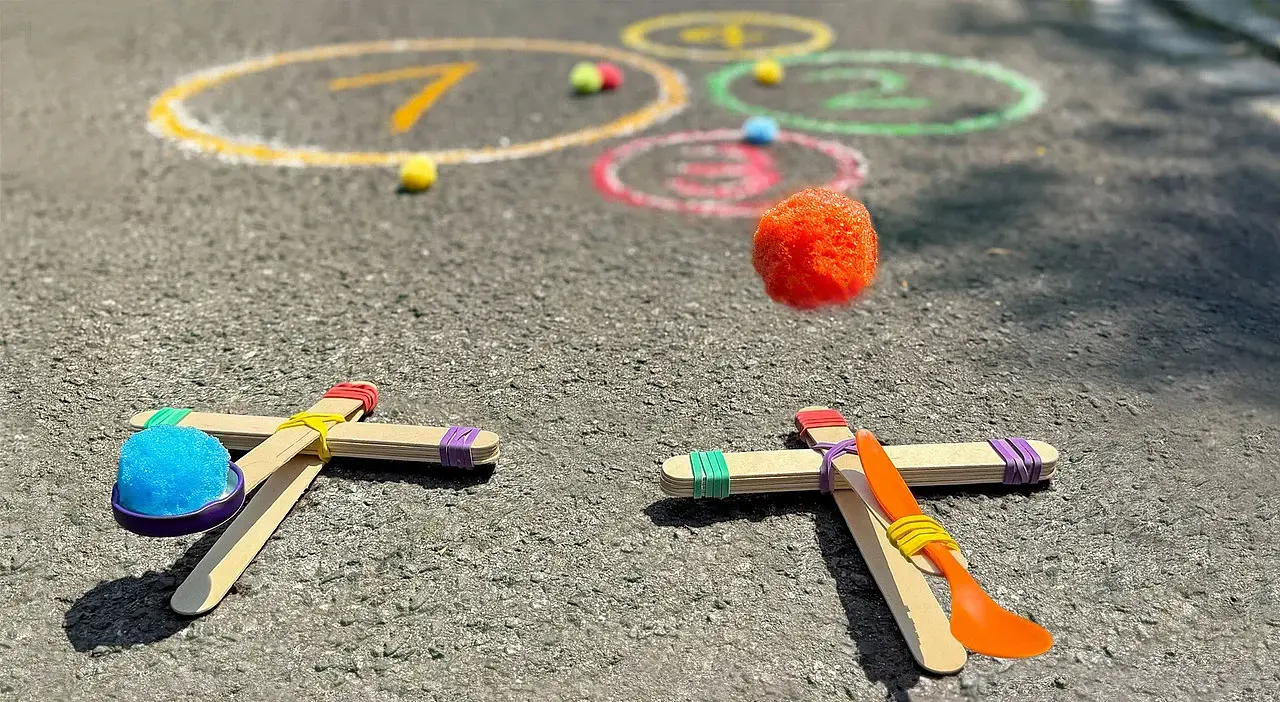 © Ina Kerckhoff Zwei selbstgebaute Katapulte aus Holzstäbchen und Haushaltsgummis: Von einem fliegt ein Schwämmchen durch die Luft Richtung Kreide-Kreise auf der Straße.