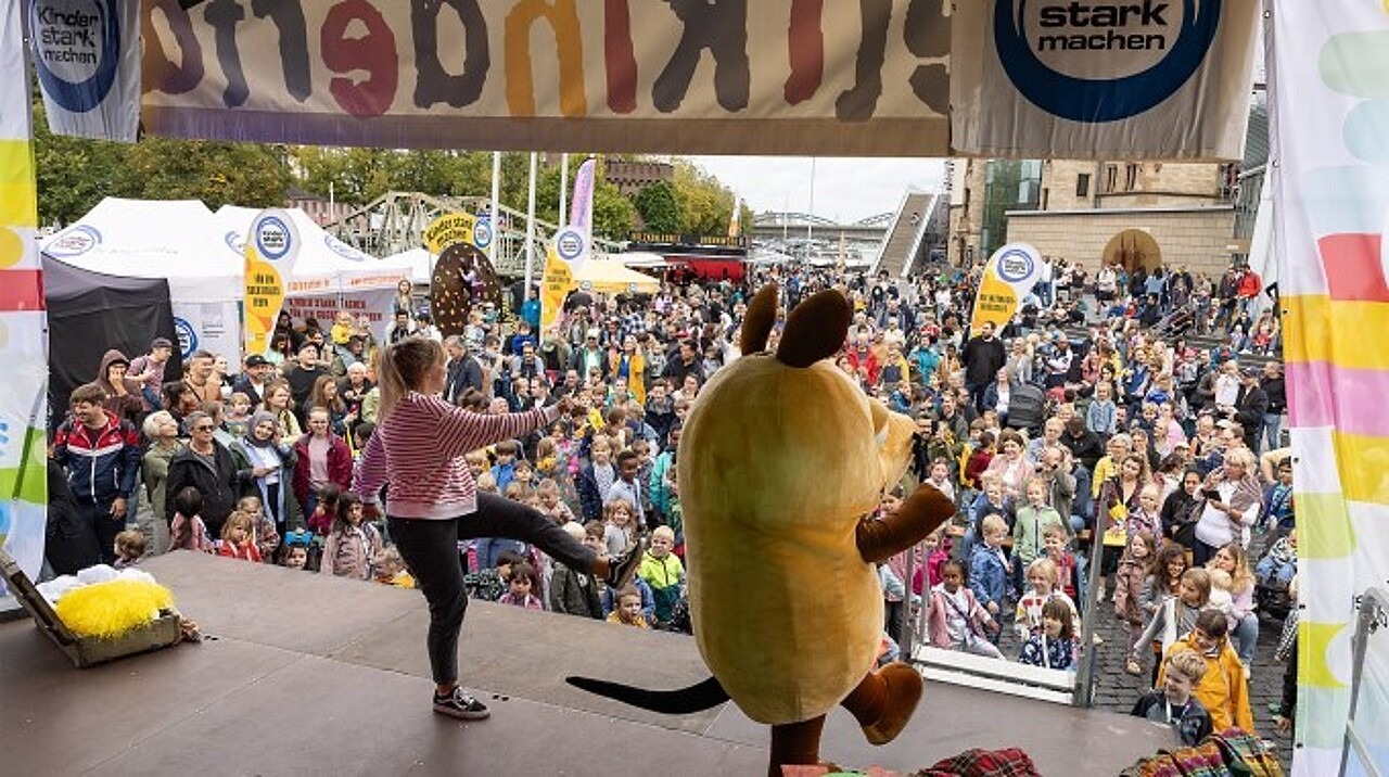 Maus schaut auf das große vor der Bühne versammelte Publikum