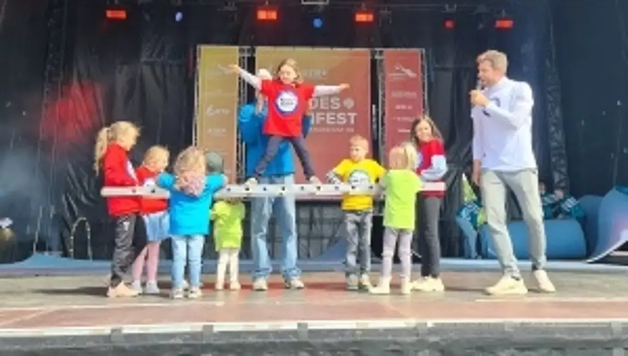 Kinder auf der Hauptbühne mit dem „Kinder stark machen“-Team. Die Kinder halten eine Leiter waagerecht und ein Mädchen steht freihändig auf der Leiter.