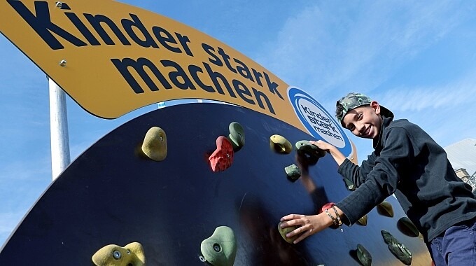 Junge klettert auf der drehbaren „Kinder stark machen“-Kletterscheibe