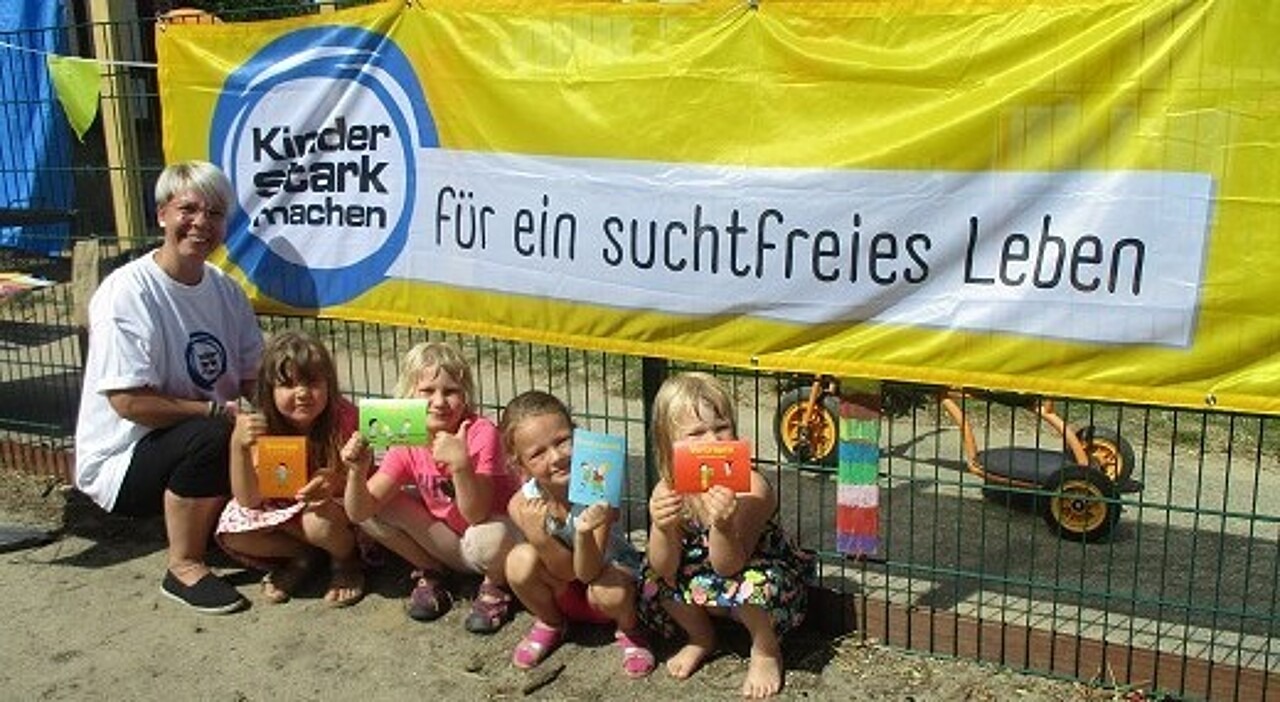 Kinder und eine Erzieherin der Kita Mühlenspatzen vor einem "Kinder stark machen"-Banner