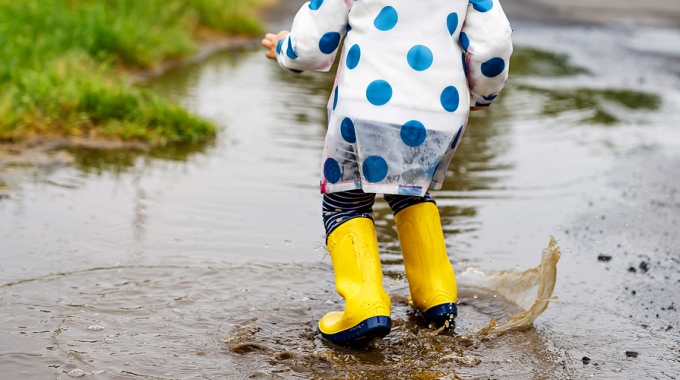 Ein Kind mit Gummistiefeln und Regenjacke springt in eine Pfütze