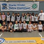 Eine Gruppe Kinder des TSV Achim steht mit ihrem Trainer vor einem "Kinder stark machen"-Banner
