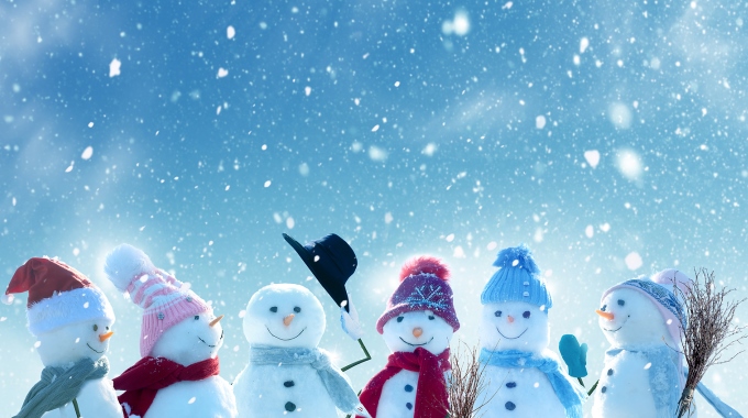 Sechs freundliche Schneemänner mit Pudelmützen im Schneetreiben. Einer zieht seinen Hut.