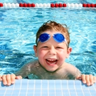 Ein vor Vergnügen lachender Junge mit Schwimmbrille im Freibad.