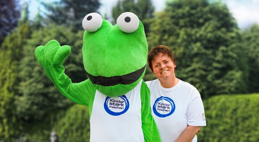 Turni Turnfrosch & Birgit Kleinschmidt Maskottchen „Turni Turnfosch“ & Übungsleiterin Birgit Kleinschmidt im „Kinder stark machen“-T-Shirt