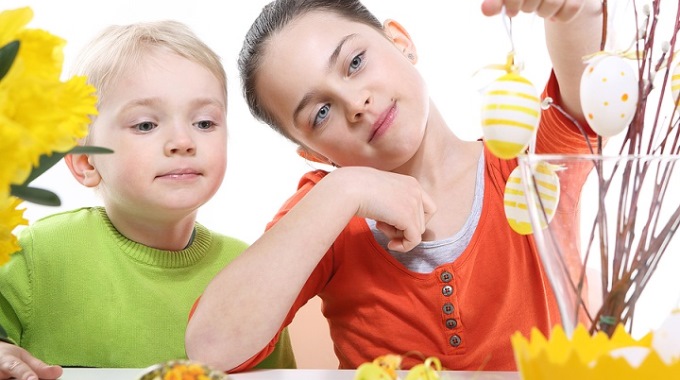 Ein Mädchen und ein Junge hängen Ostereier an Weidenkätzchen-Zweige in einer Vase.