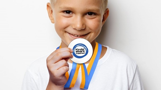 Ein Junge zeigt seine „Kinder stark machen"-Medaille.