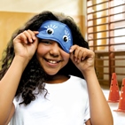 Ein Mädchen in der Turnhalle hebt die Augenbinde leicht an und lächelt darunter hervor.