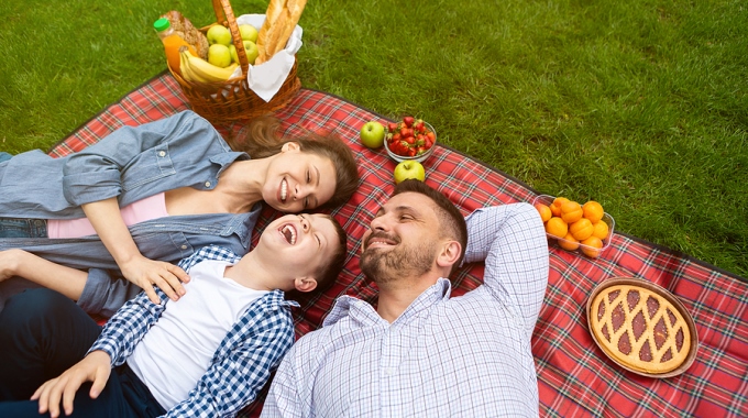 Mutter, Sohn und Vater liegen auf rot-karierter Picknickdecke und strahlen.