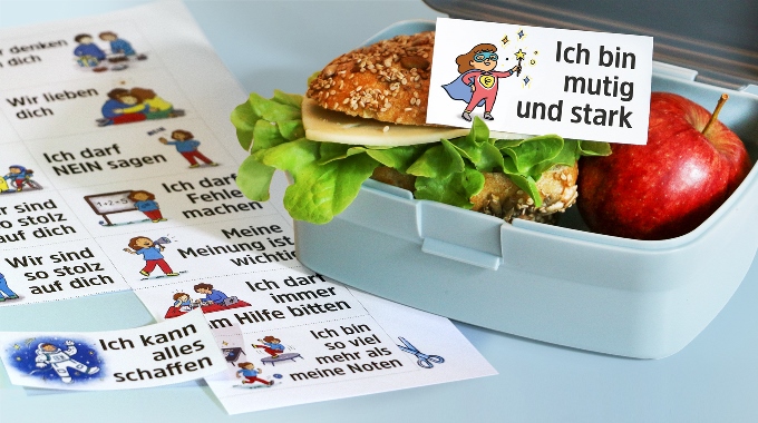 ©  Illustration Eva Burckhardt, Composing Ina Kerckhoff „Ich bin mutig und stark“ ist auf der Botschaft zu lesen, die auf einem mit Käse und Salat belegten Brötchen in einer geöffneten Brotdose liegt.