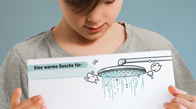 Ein Junge zeigt die PDF-Vorlage für die Warme Dusche mit einem Bild von einem Duschkopf, darunter viel Platz für positive Botschaften.