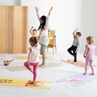 Kinder stehen im Kreis mit ihrer Betreuerin auf Yogamatten mit Tiermotiven und üben sich im Einbeinstand.